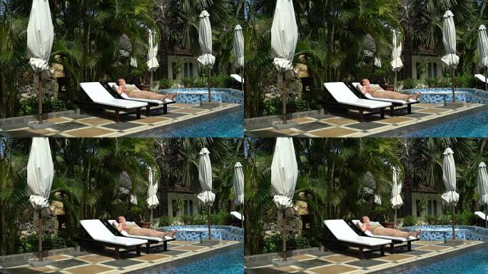 穿着游泳池旁的泳衣的女人躺在日光浴躺椅上，晒成黑呢