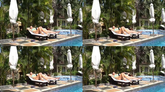 穿着游泳池旁的泳衣的妇女躺在日光浴躺椅上，晒日光浴