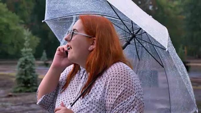 情感胖姜带眼镜女孩站在雨下公园，打电话，撑伞，沟通理念