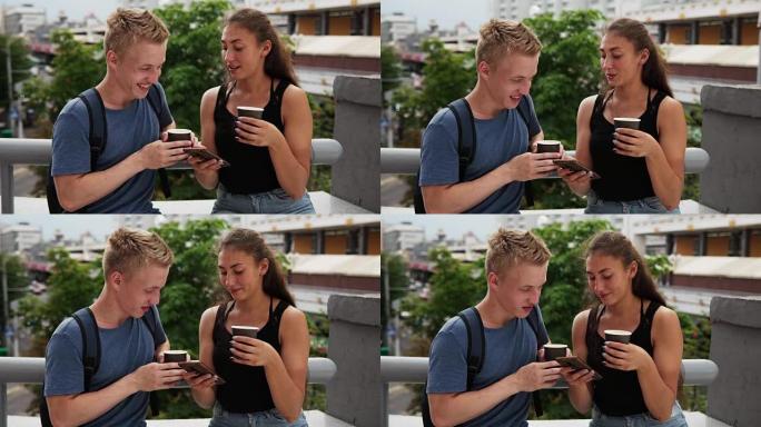 年轻的幸福夫妇在城市街喝咖啡并使用智能手机
