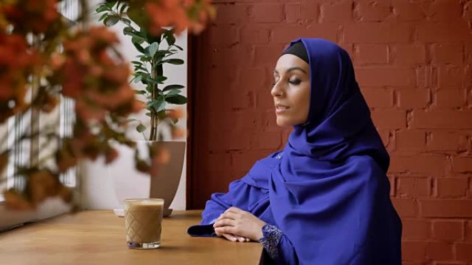 年轻的穆斯林妇女戴着头巾，对着镜头微笑，坐在咖啡馆里，鼻子穿孔的女性