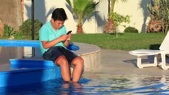 在游泳池附近使用智能手机的小男孩