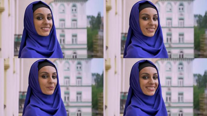 戴着头巾的年轻迷人穆斯林妇女看着相机，微笑着站在街上