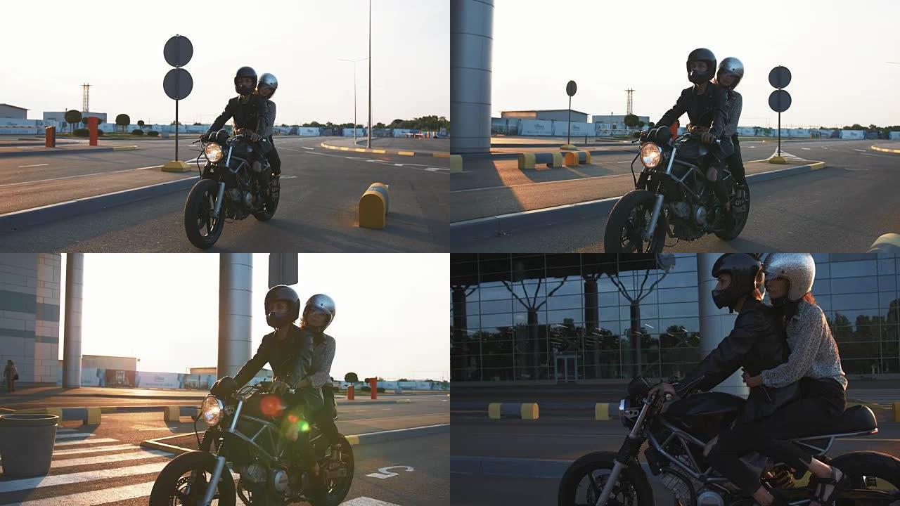 日落时，戴着头盔的年轻夫妇在城市骑摩托车，慢动作