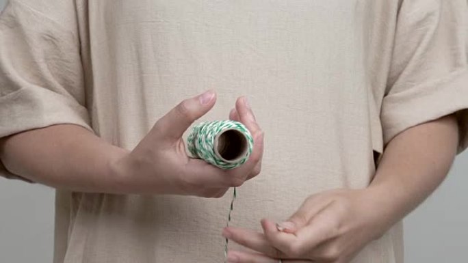 女人的手拿着一卷条纹绳的特写镜头。她拉绳子，解开它，然后把它卷回去。