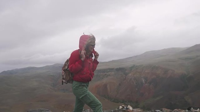 年轻女子游客在山里大雨下行走。背着背包的女孩旅行者在恶劣的天气中挣扎