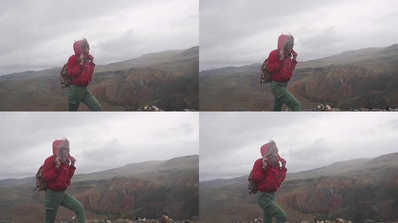年轻女子游客在山里大雨下行走。背着背包的女孩旅行者在恶劣的天气中挣扎
