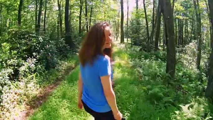 这位16岁的白人白人，长发，女孩在森林小径上徒步旅行，回头看着挥手。