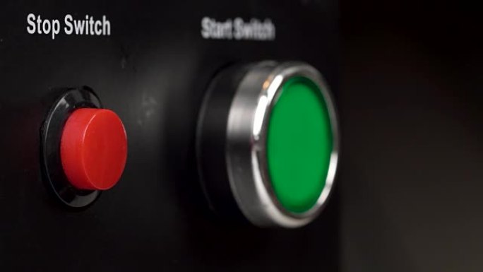 框架中两个按钮的特写。绿色启动开关和红色停止开关按钮。手指按下红色停止开关按钮。