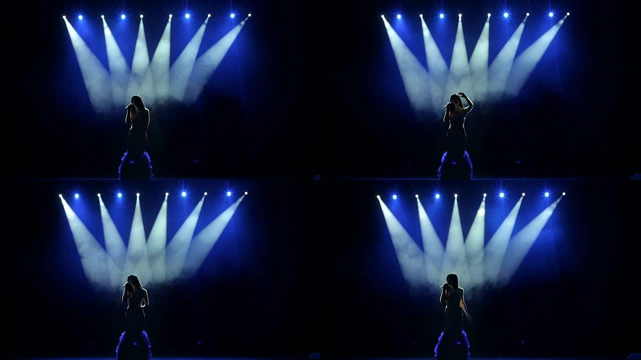 美丽的歌手在黑暗中的舞台上唱歌。