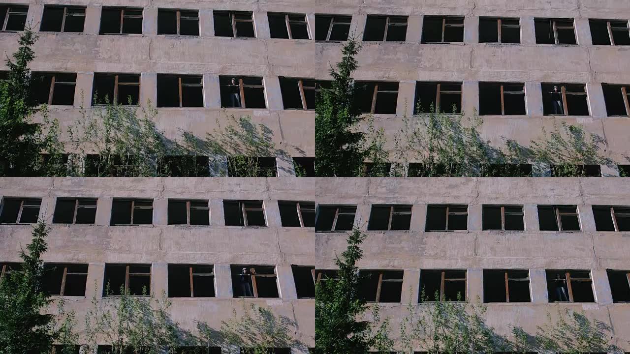 女人站在被毁的多层建筑的窗户上，窗户很多破了。
