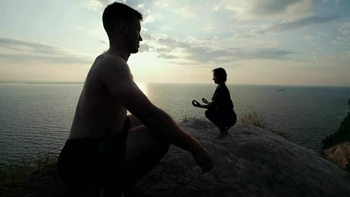 青年男女在日出时在大石头上练习瑜伽