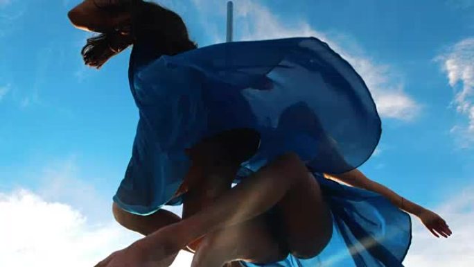 两名身穿蓝色裙子的钢管女舞者在塔尖上对着天空表演舞蹈