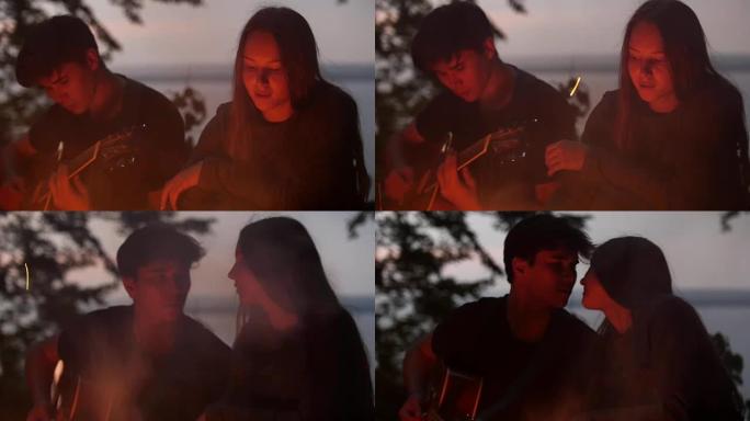 年轻的情侣坐在篝火旁，在森林里弹吉他