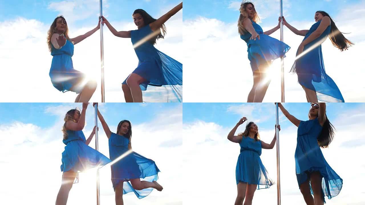 两名身穿蓝色连衣裙的年轻女舞者在蓝天下表演钢管舞