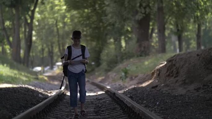 旅行者男孩正沿着铁轨行走，看着地图，男孩沿着正确的方向走铁路