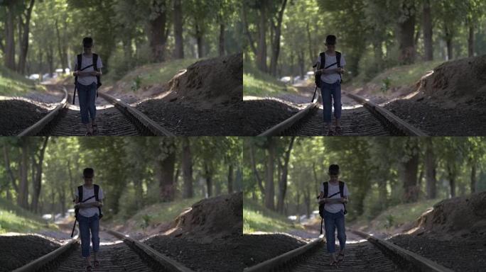 旅行者男孩正沿着铁轨行走，看着地图，男孩沿着正确的方向走铁路