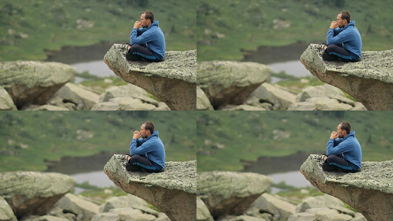 一个年轻人坐在悬崖边吹口琴。