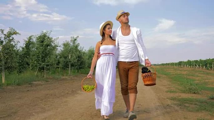 恋爱中的夫妇在野外享受新鲜空气，戴着草帽，带着一篮子水果和一只小狗在大自然中行走