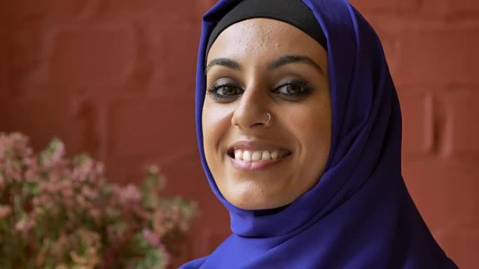 年轻的穆斯林妇女戴着头巾，鼻子穿孔，看着照相机和微笑，美丽快乐的女士肖像