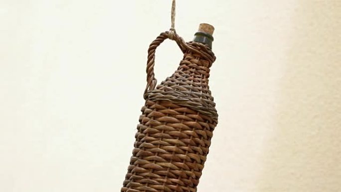 一个古老的，时尚的柳条酒瓶，挂在酒窖前的绳子上。