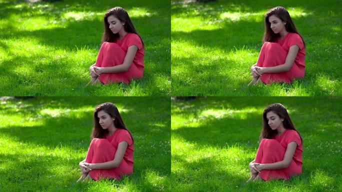 一个美丽的年轻女子坐在草地上。她护理膝盖。摄像机从左到右缓慢移动。