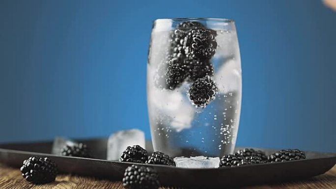 将透明的苏打水倒入装有黑莓和冰的玻璃杯中。排毒水概念。