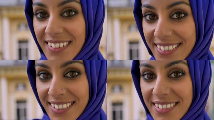 年轻的穆斯林妇女在雨中对着镜头微笑的肖像，鼻子被刺穿的美丽女性