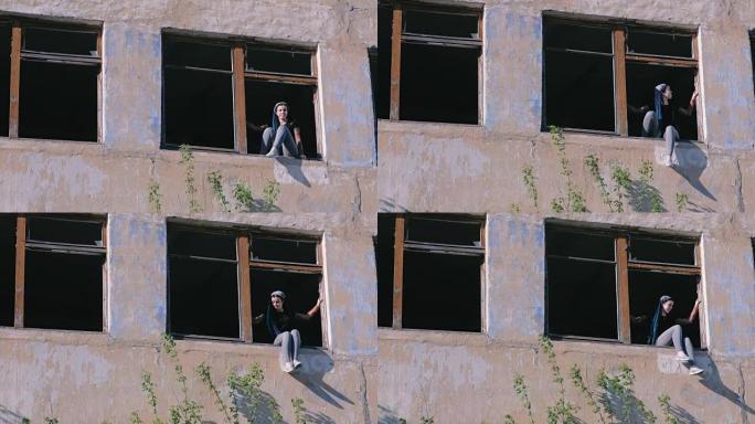女人坐在被毁的多层建筑的窗户上，窗户很多破了。