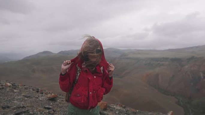 背着背包的女孩旅行者在恶劣的天气中挣扎。年轻女子游客在山里大雨下行走。