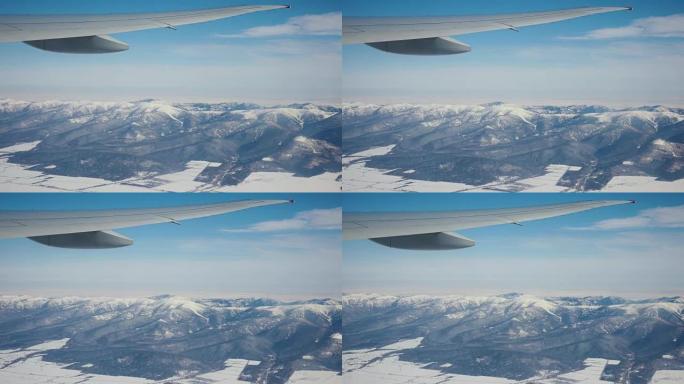 从飞机的窗户拍摄，飞机在白雪覆盖的山脉上飞行