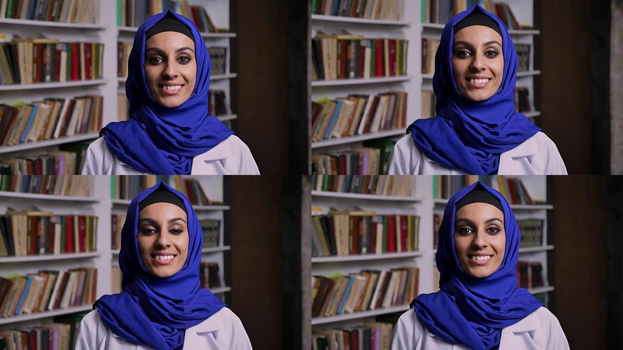戴着头巾的年轻美丽的穆斯林妇女站在图书馆，带着幸福的表情对着镜头微笑