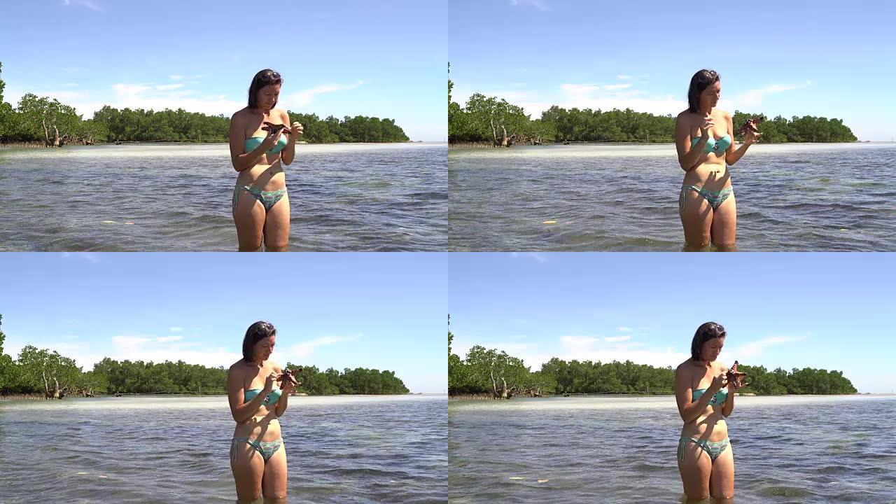 一个穿着泳衣的女人站在海里，手里拿着海星