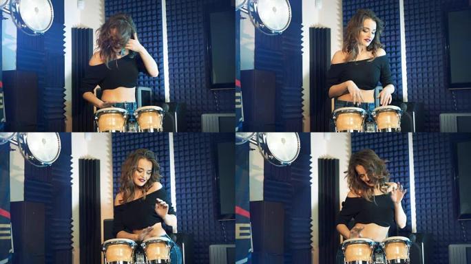 穿着牛仔裤和上衣的有趣女人在专业设备的背景下在音频工作室打鼓和跳舞。