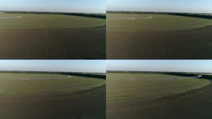 农作物除尘器在田间飞来，用小麦和飞溅的化学物质抵御寄生虫，在老式推进飞机的无人机视图中，在种植园上空