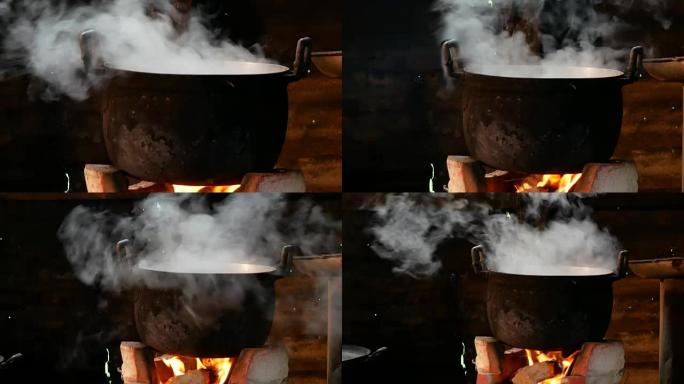 土炉和柴火上有蒸汽的黑色烹饪锅锅
