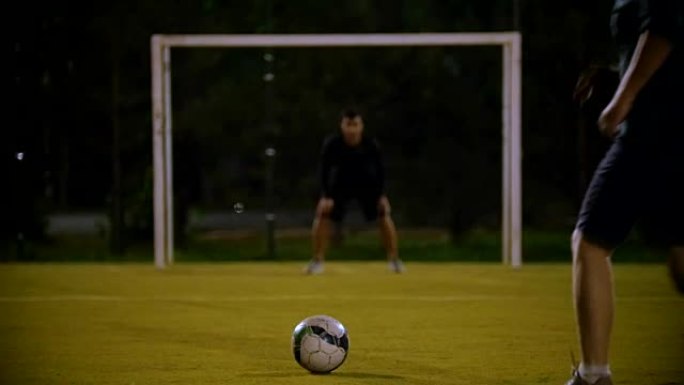 球躺在前景的草地上，守门员在门口，另一名球员踢球，但没有击中球门