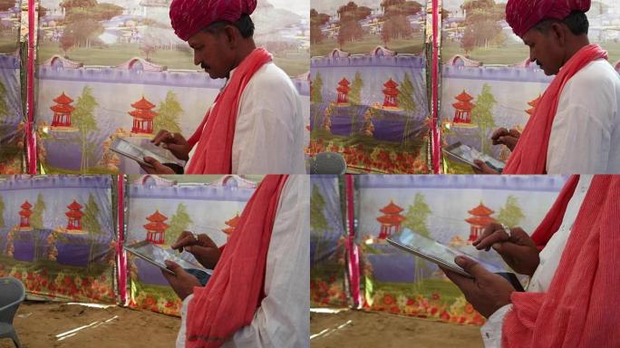 手持印度男子忙于触摸屏平板电脑，配有色彩鲜艳的帐篷背景
