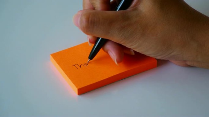 在橙色的便签纸或记事本上手写 “谢谢” 一词