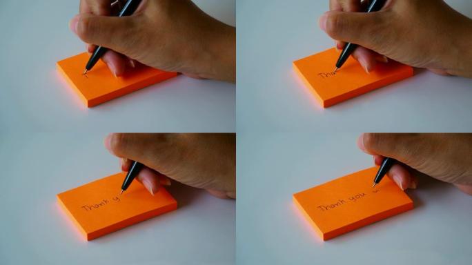 在橙色的便签纸或记事本上手写 “谢谢” 一词