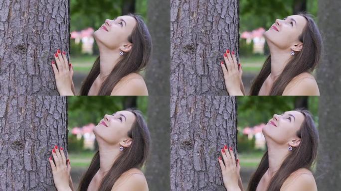 漂亮的女士微笑着看着树，快乐的女人在一棵大树下享受大自然