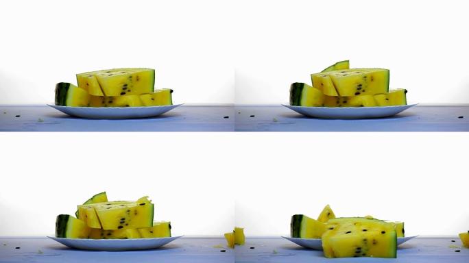 桌上的黄色西瓜切片。另一片从上方落下
