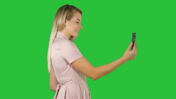 年轻漂亮的女人在绿屏上的手机上自拍，色键