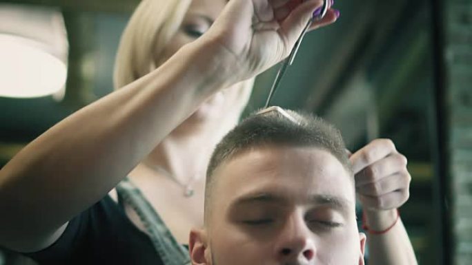 女发型师在理发店用剪刀和梳子剪掉年轻人的头发。慢动作中的理发过程。特写。