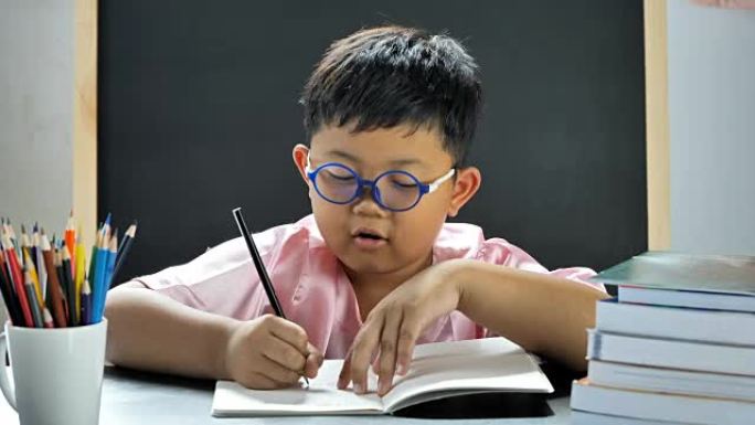 可爱的亚洲小男孩思考并写进书中，开心地在家里微笑。教育理念