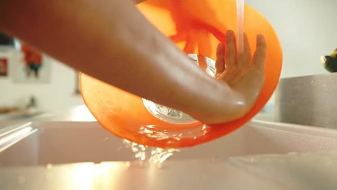 雌性用手用光学耀斑在水龙头慢动作高清镜头下洗橙色碗。