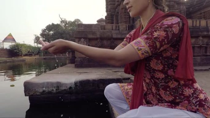 年轻的印度妇女在祭品中举起神圣的水，慢动作，背景是寺庙。