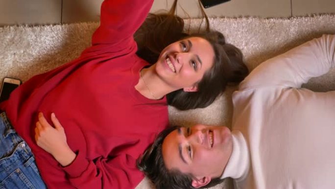 年轻美丽的夫妇在地毯上正面交锋，在舒适的氛围中使用智能手机制作自拍照片。