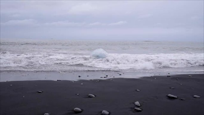 在Jokulsarlon Diamond's beach的冰岛黑沙滩上，海浪在冰山上飞溅的慢动作视频