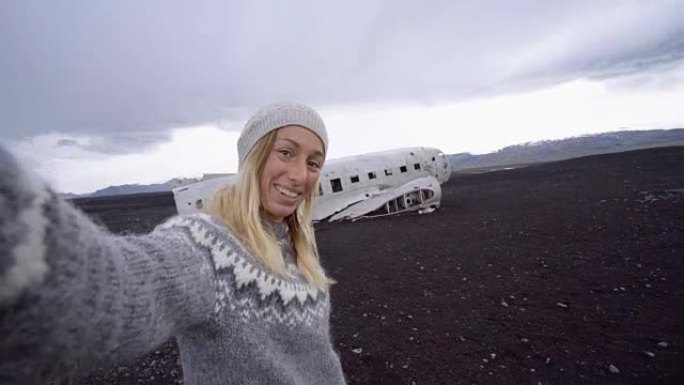 4k的年轻女子站在飞机残骸旁，在黑沙滩上自拍，这是冰岛著名的景点，并与残骸合影